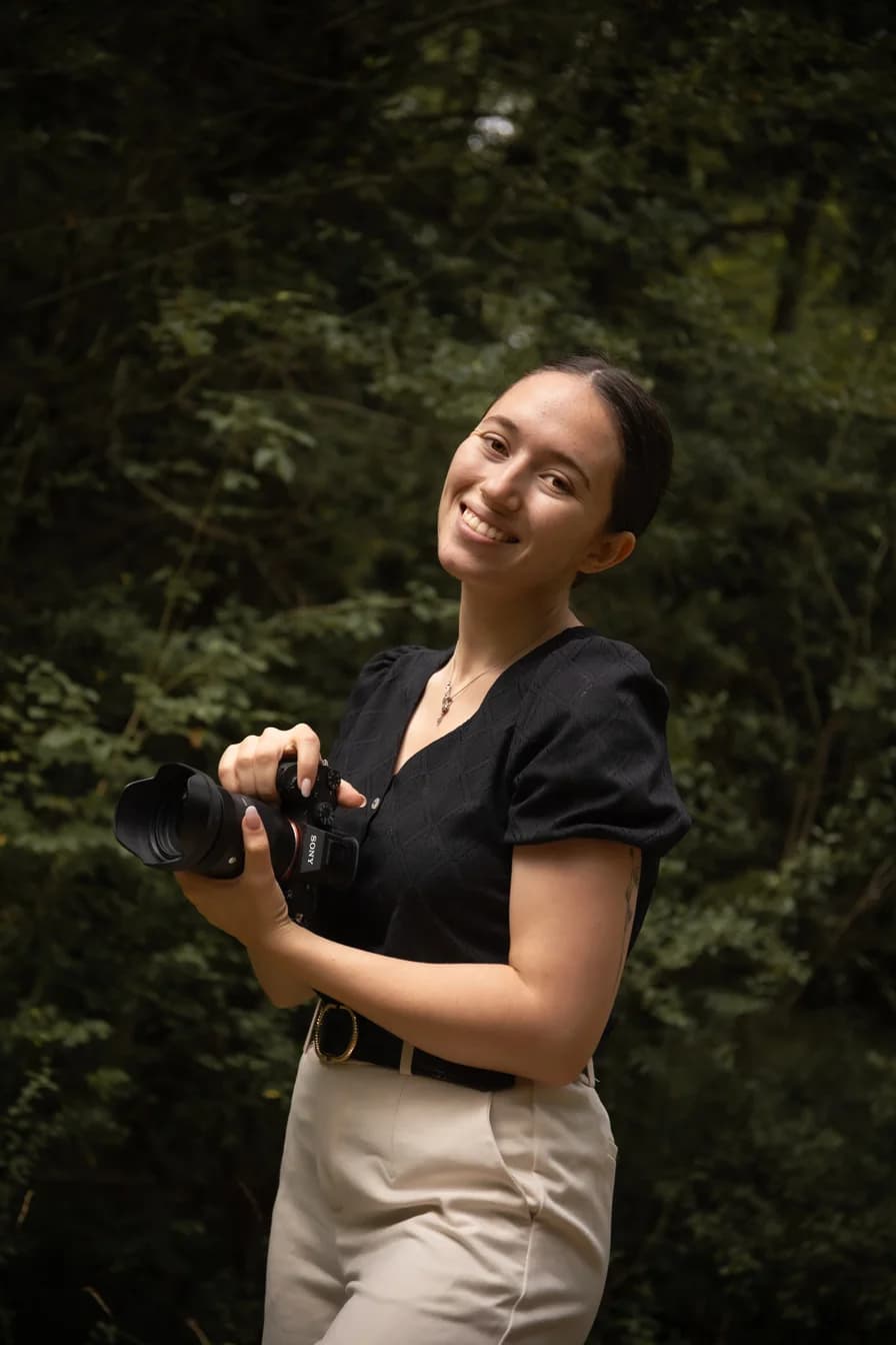 Elia Grimaud holding a camera, smiling in a forest